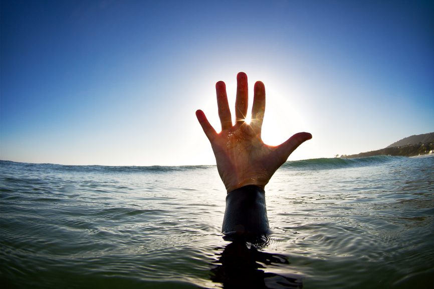 A hand reaching up out of the surface of the ocean with late afternoon light.